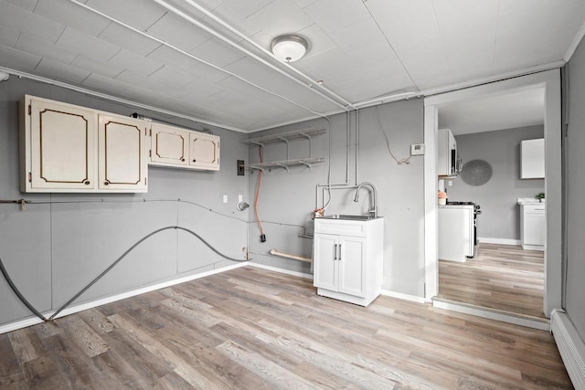 basement featuring a baseboard heating unit, light hardwood / wood-style flooring, and sink