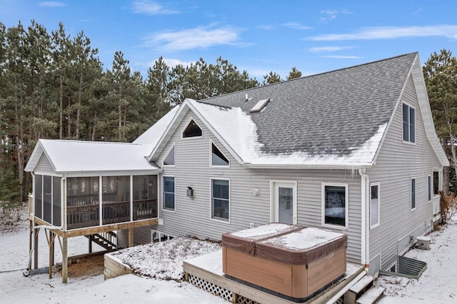 snow covered back of property featuring a hot tub and a sunroom