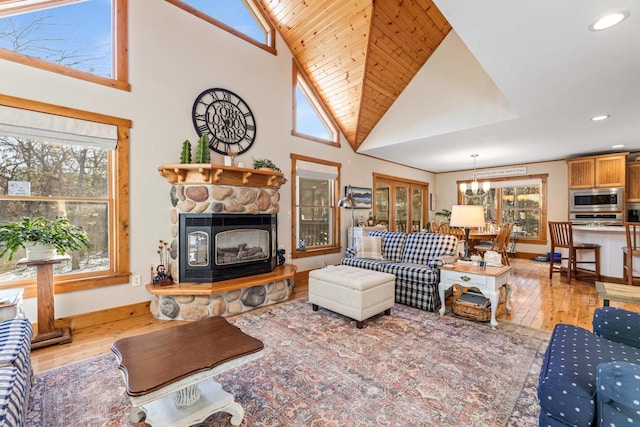 living room with high vaulted ceiling, a stone fireplace, light hardwood / wood-style floors, and a notable chandelier