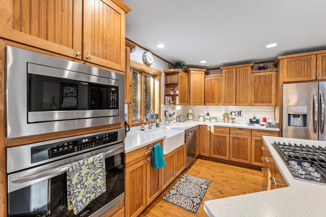 kitchen with appliances with stainless steel finishes, sink, backsplash, and light hardwood / wood-style flooring