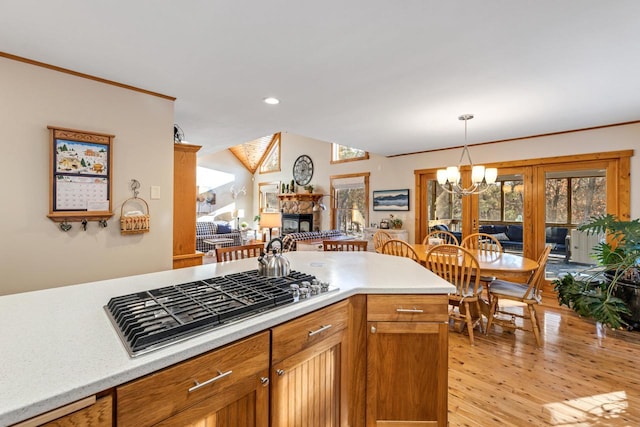 kitchen with a fireplace, decorative light fixtures, stainless steel gas stovetop, a notable chandelier, and light hardwood / wood-style floors