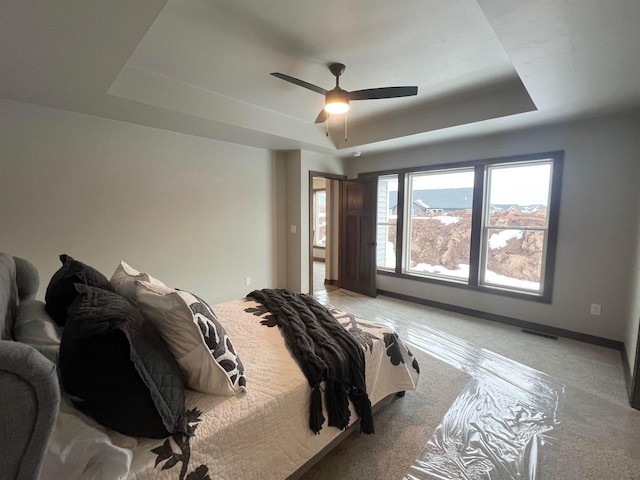 bedroom featuring light carpet, a tray ceiling, visible vents, and baseboards