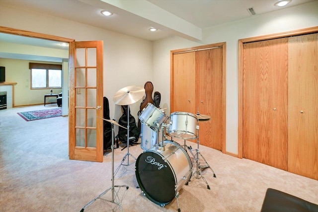 miscellaneous room with beamed ceiling, a tiled fireplace, light carpet, and french doors