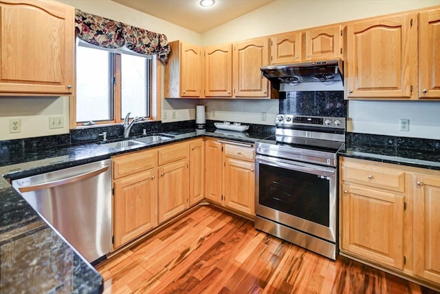 kitchen featuring vaulted ceiling, sink, dark stone countertops, stainless steel appliances, and light hardwood / wood-style flooring