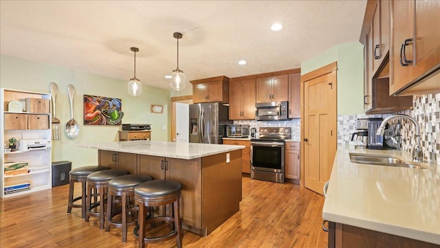 kitchen with sink, light stone counters, decorative light fixtures, a center island, and appliances with stainless steel finishes