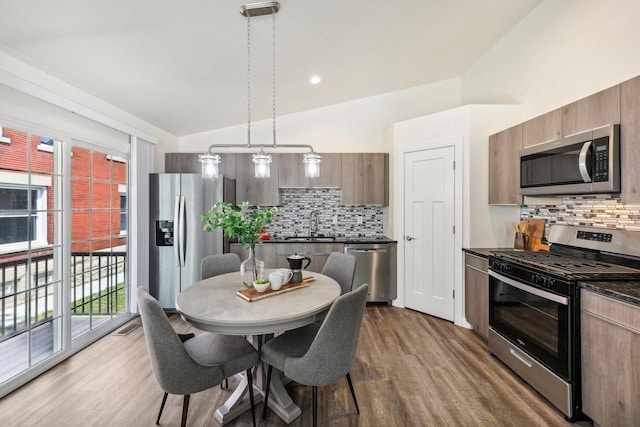 kitchen with sink, hardwood / wood-style flooring, hanging light fixtures, stainless steel appliances, and vaulted ceiling