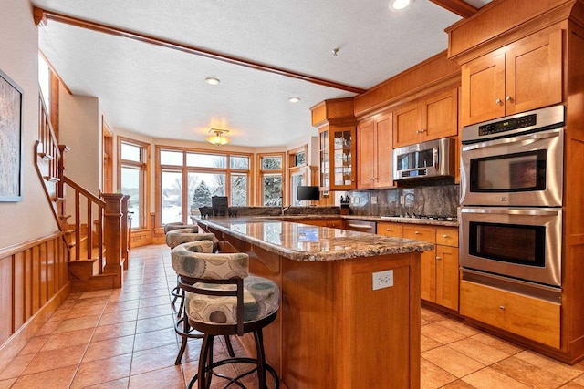 2532 Huntington Way, Suamico, WI 54173 - kitchen with stainless steel appliances, a breakfast bar, a textured ceiling, and brown cabinetry