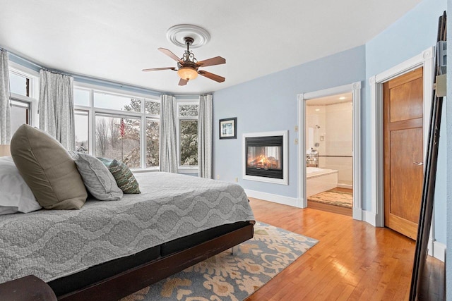 2532 Huntington Way, Suamico, WI 54173 - bedroom with light wood finished floors, a ceiling fan, a multi sided fireplace, connected bathroom, and baseboards