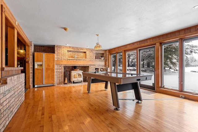 2532 Huntington Way, Suamico, WI 54173 - rec room featuring brick wall, a wood stove, a textured ceiling, and light wood-style floors