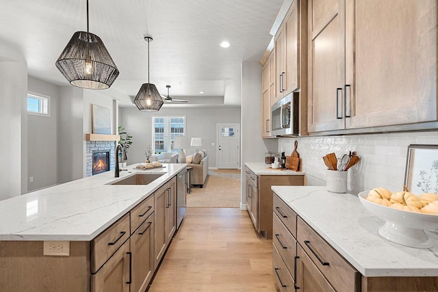 kitchen featuring a stone fireplace, pendant lighting, sink, stainless steel appliances, and a spacious island