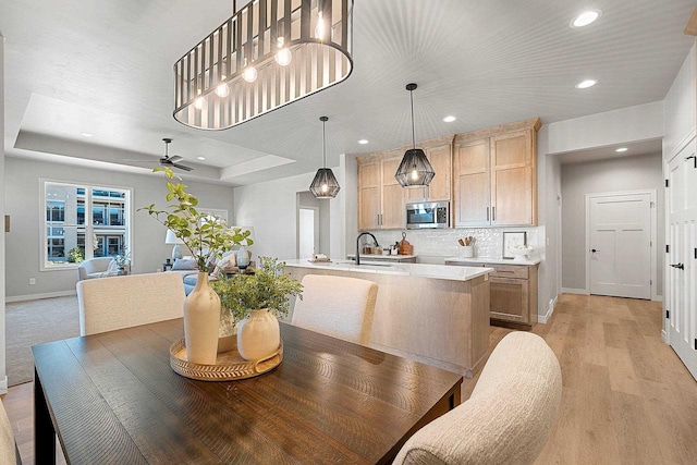 dining space with sink, a tray ceiling, ceiling fan, and light wood-type flooring