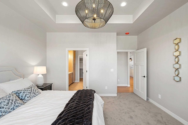 bedroom featuring light colored carpet, ensuite bathroom, and a raised ceiling