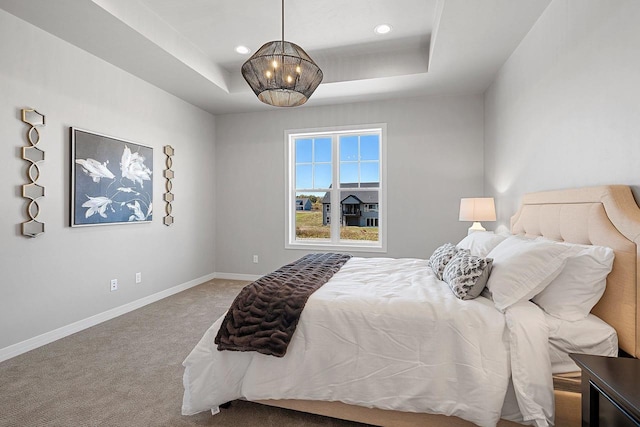 bedroom with a tray ceiling, a chandelier, and carpet