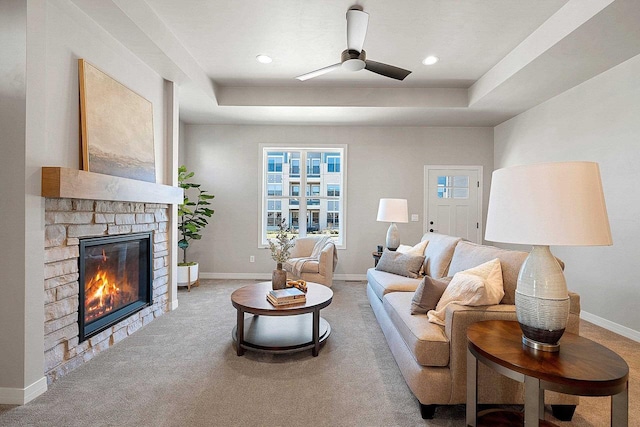 living room with ceiling fan, a fireplace, a raised ceiling, and carpet flooring