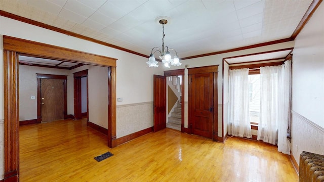 empty room featuring ornamental molding, radiator heating unit, a chandelier, and light wood-type flooring