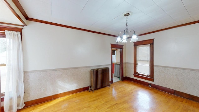 spare room with hardwood / wood-style flooring, radiator heating unit, crown molding, and a chandelier