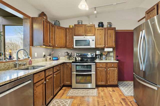 kitchen with stainless steel appliances, lofted ceiling, sink, and light hardwood / wood-style flooring