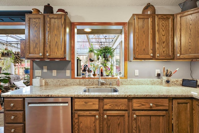 kitchen with plenty of natural light, dishwasher, sink, light stone countertops, and a textured ceiling