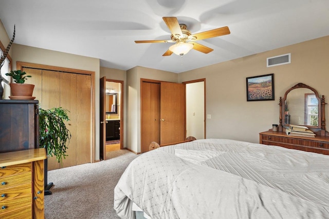 carpeted bedroom featuring multiple closets, connected bathroom, and ceiling fan