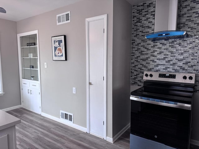 kitchen with wall chimney exhaust hood, stainless steel electric range oven, light hardwood / wood-style floors, and decorative backsplash