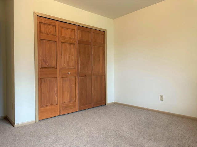 unfurnished bedroom with light colored carpet and a closet