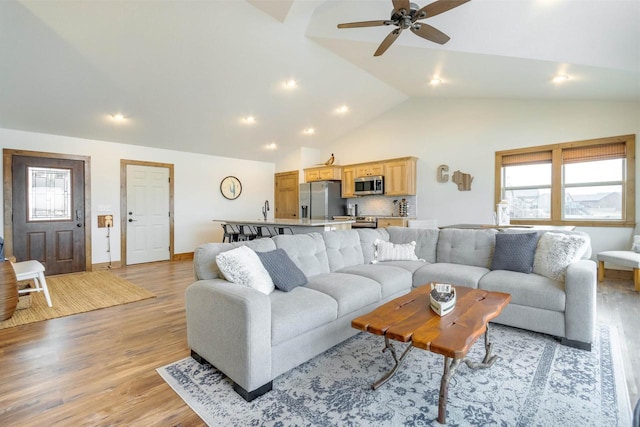 living room with ceiling fan, high vaulted ceiling, and light hardwood / wood-style flooring