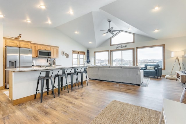 kitchen with a breakfast bar area, light hardwood / wood-style flooring, a large island with sink, stainless steel appliances, and backsplash