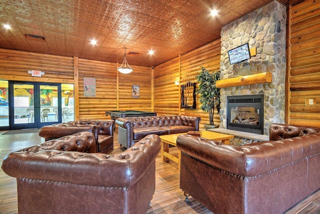 living room with french doors, a stone fireplace, rustic walls, and hardwood / wood-style floors