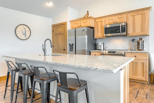 kitchen featuring appliances with stainless steel finishes, an island with sink, sink, backsplash, and light hardwood / wood-style flooring