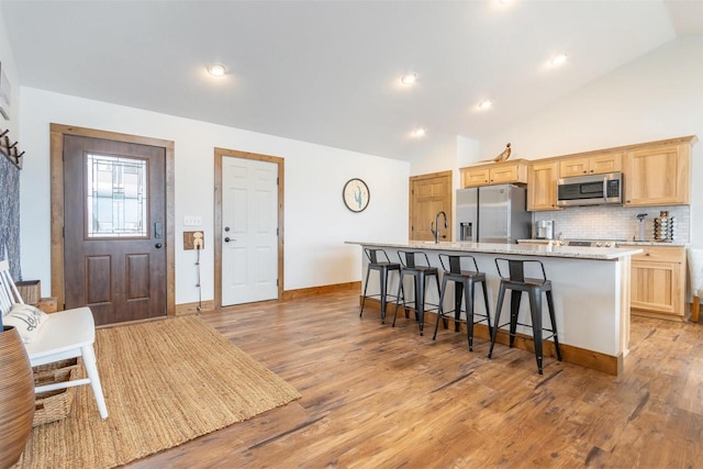 kitchen featuring a breakfast bar area, light brown cabinets, stainless steel appliances, a center island with sink, and light wood-type flooring