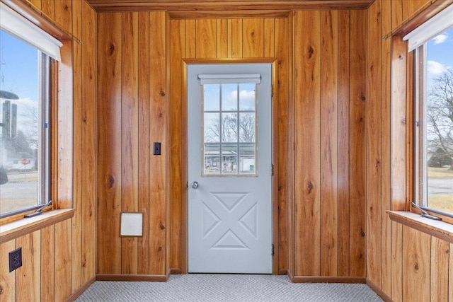 doorway featuring light colored carpet, wooden walls, and a wealth of natural light