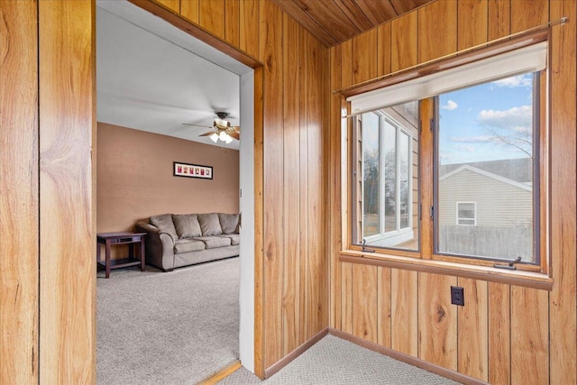 doorway to outside with wood walls, ceiling fan, and carpet