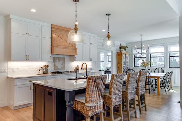 kitchen with pendant lighting, sink, light hardwood / wood-style flooring, white cabinetry, and an island with sink