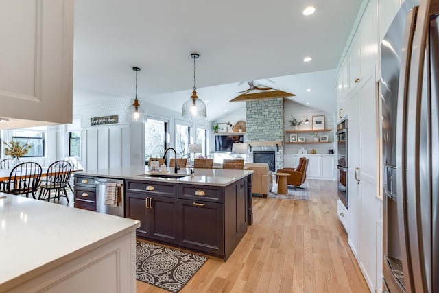 kitchen with sink, appliances with stainless steel finishes, hanging light fixtures, a fireplace, and white cabinets