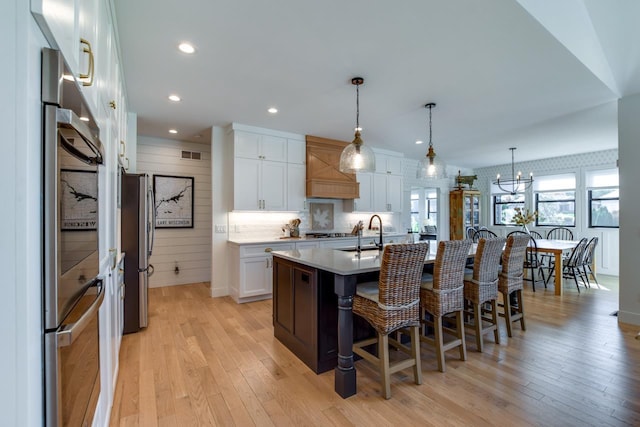 kitchen featuring pendant lighting, an island with sink, white cabinets, and appliances with stainless steel finishes