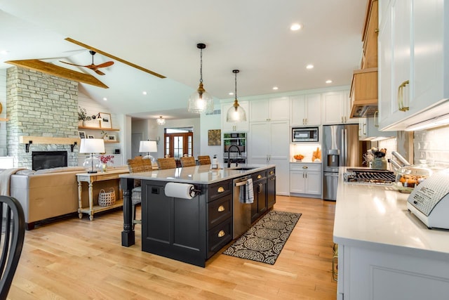 kitchen featuring white cabinetry, stainless steel appliances, an island with sink, and hanging light fixtures