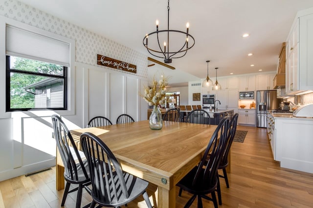 dining space with an inviting chandelier, sink, and light hardwood / wood-style flooring