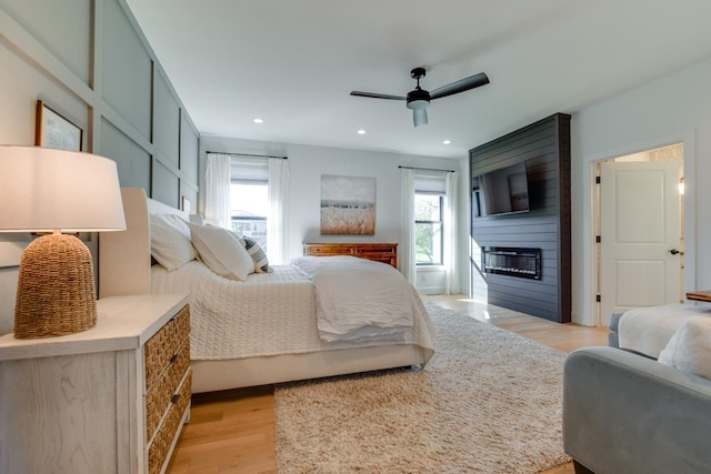 bedroom with a large fireplace, ceiling fan, and light wood-type flooring