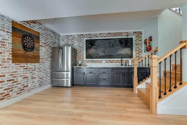 interior space with sink, light wood-type flooring, stainless steel refrigerator, and brick wall