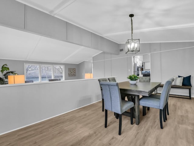 dining area with an inviting chandelier, vaulted ceiling, and light hardwood / wood-style flooring