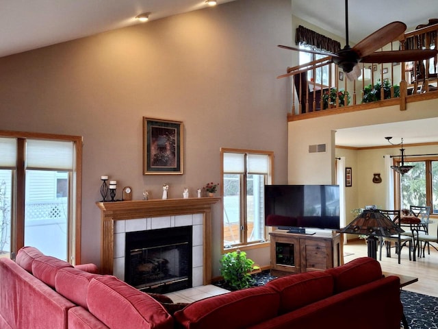 living room with light hardwood / wood-style flooring, ornamental molding, a tile fireplace, a towering ceiling, and ceiling fan