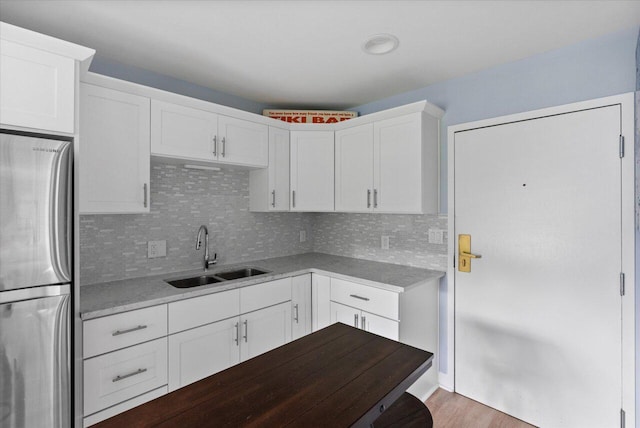 kitchen featuring stainless steel refrigerator, tasteful backsplash, sink, white cabinets, and light stone countertops