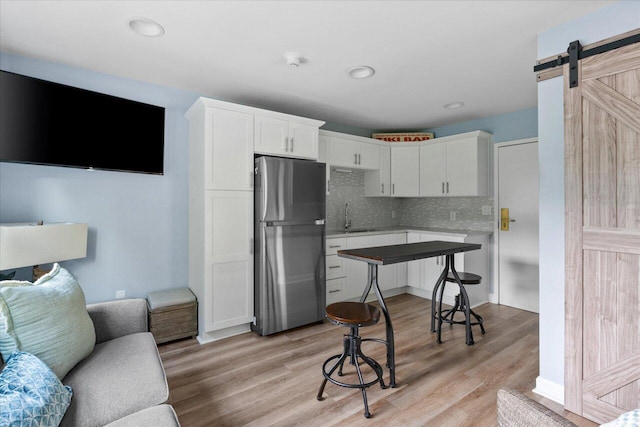 kitchen featuring white cabinetry, light wood-type flooring, stainless steel refrigerator, a barn door, and backsplash