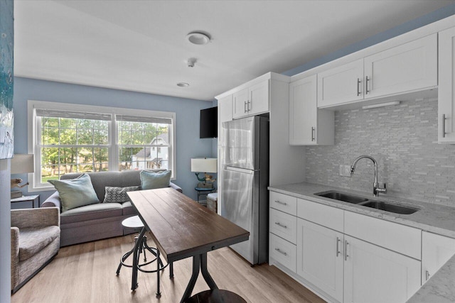 kitchen with white cabinets, sink, stainless steel fridge, and light stone counters