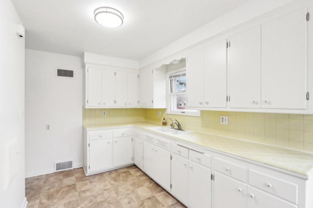 kitchen with sink, tile counters, white cabinets, and backsplash