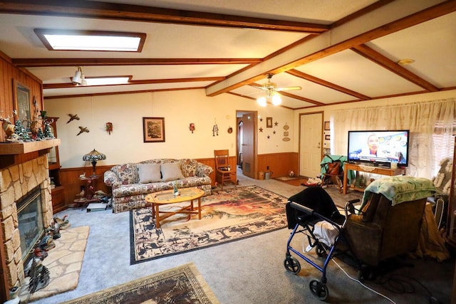 carpeted living room with a stone fireplace, lofted ceiling with beams, ceiling fan, and wood walls