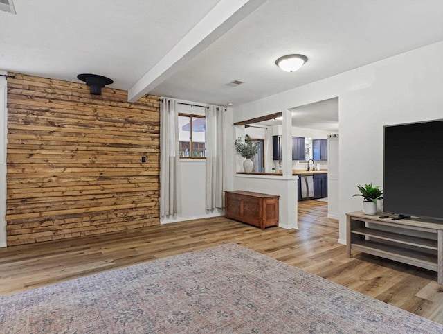 living room featuring beam ceiling, sink, and light wood-type flooring