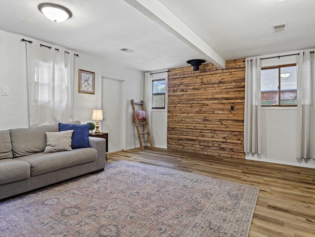 living room with beamed ceiling, wood-type flooring, wooden walls, and a textured ceiling