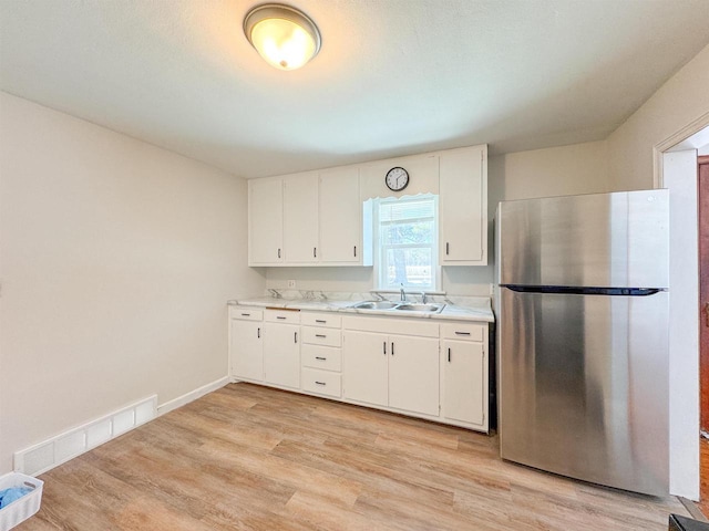 kitchen featuring white cabinetry, sink, stainless steel refrigerator, and light hardwood / wood-style floors