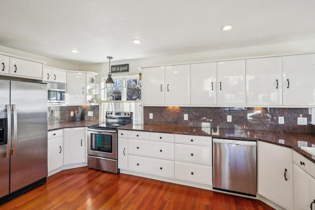 kitchen with hanging light fixtures, appliances with stainless steel finishes, dark hardwood / wood-style flooring, dark stone counters, and white cabinets